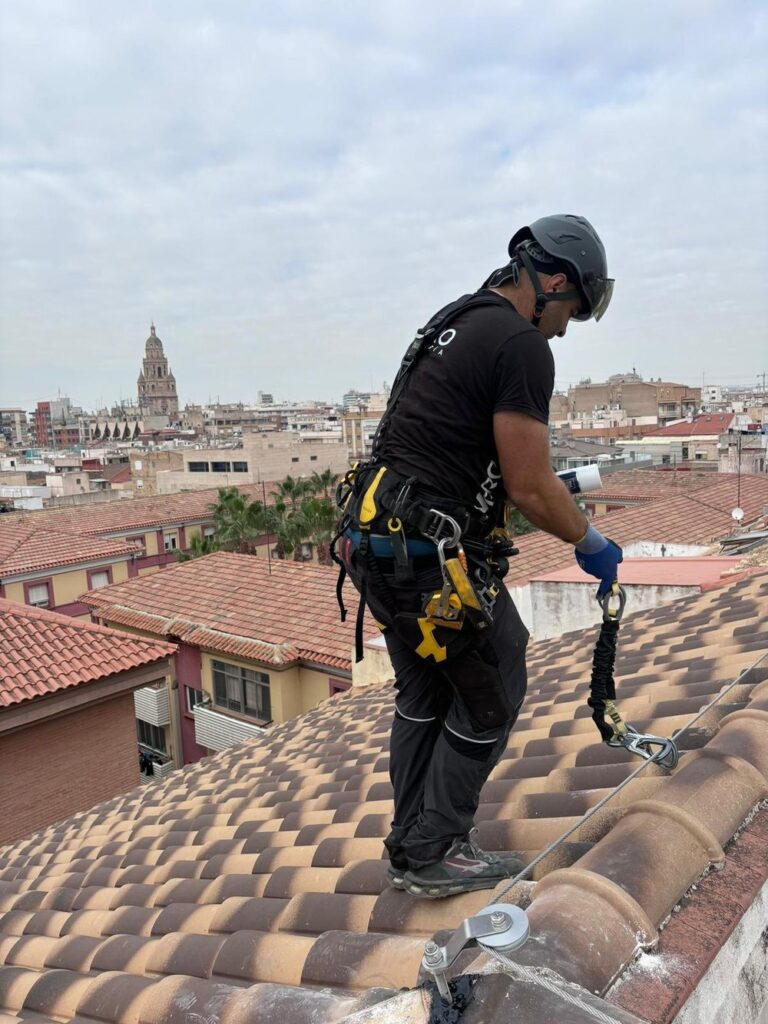 Técnico con arnés anclado trabajando sobre un tejado de teja